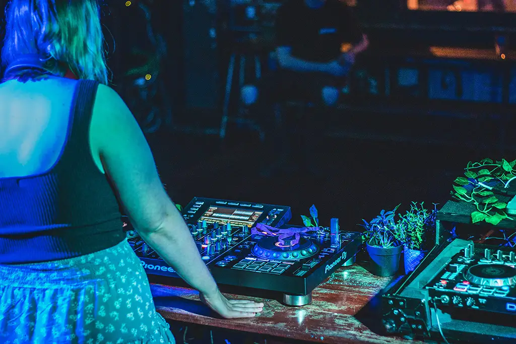 A DJ stands in front of a turntable surrounded by small potted plants.