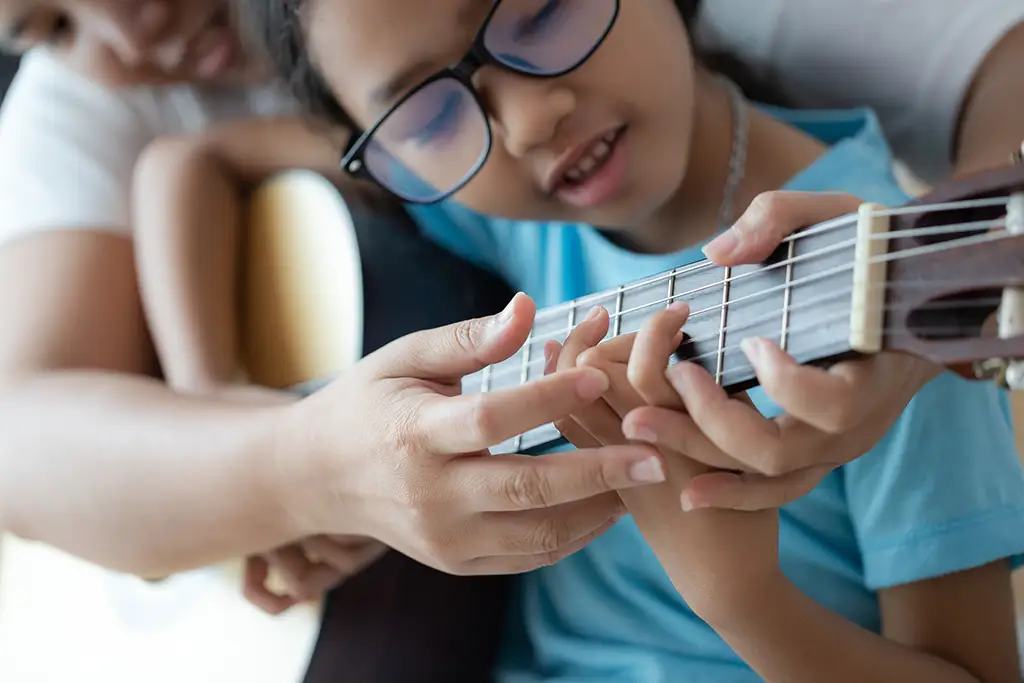 Music teacher helping student learn guitar.