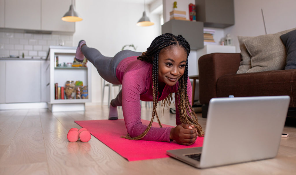 A yoga teacher walking a student through an online class by livestreaming herself on a laptop.