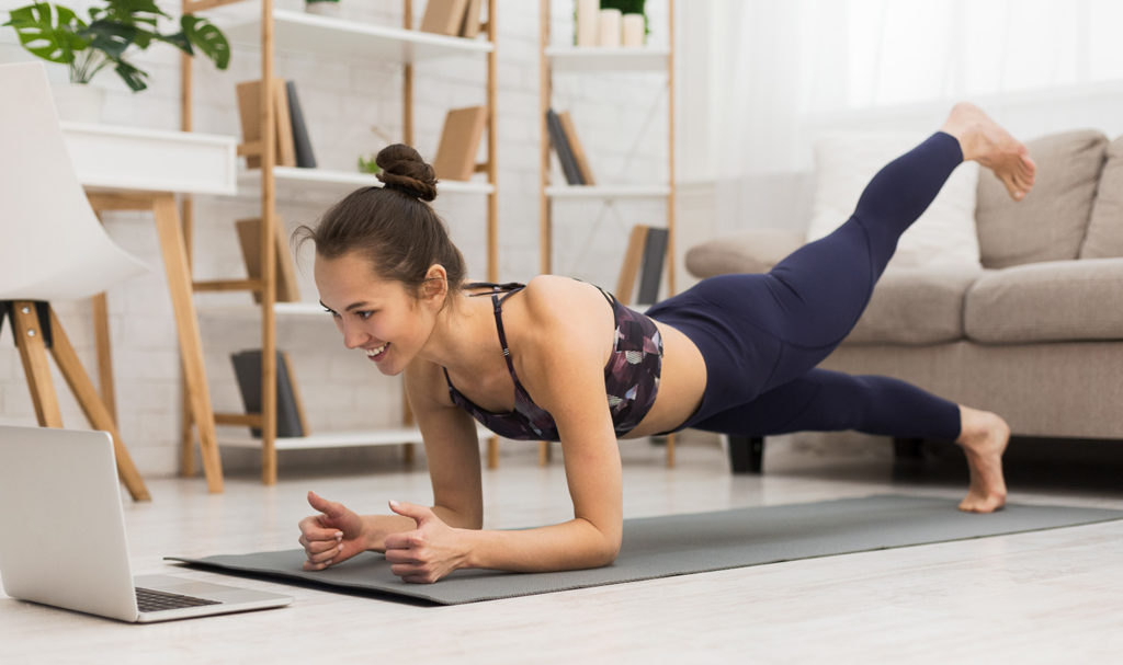 A yoga instructor is teaching a virtual client via her laptop from her home.