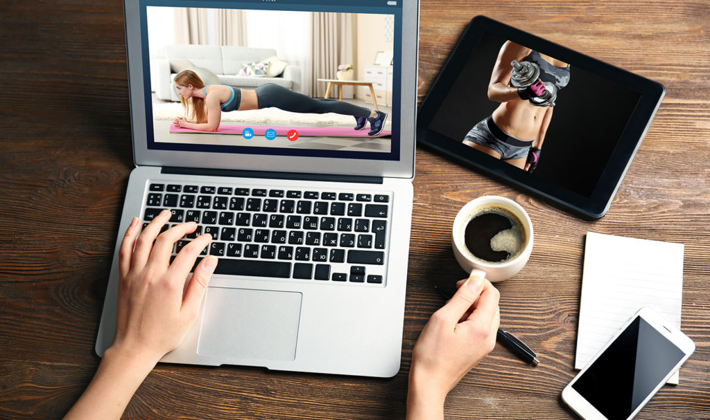 A fitness professional working on their laptop next to a tablet, a smart phone, and a cup of coffee.