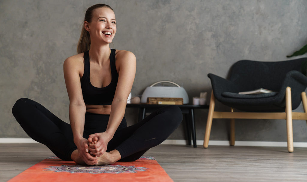A yoga student smiles and sits in a yoga pose on a mat.