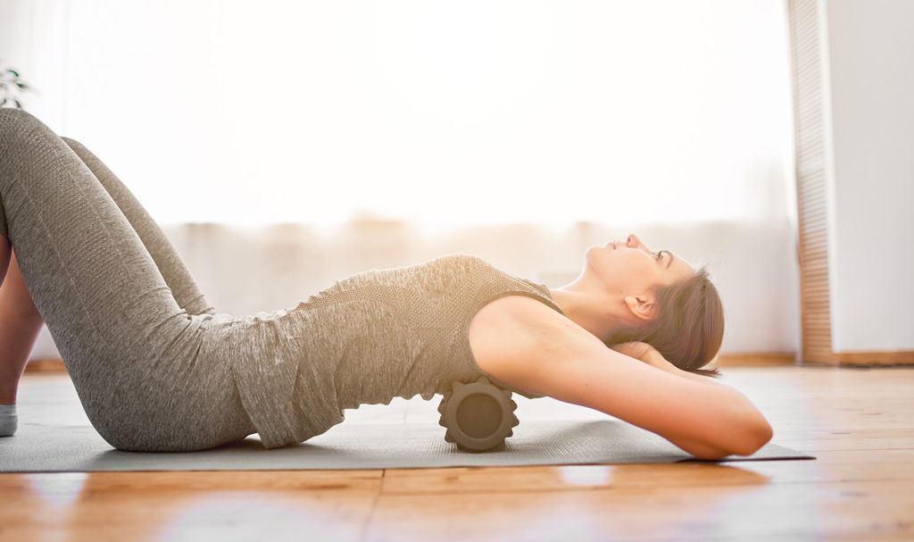 A yoga student is rolling out their back on the ground with a muscle roller.