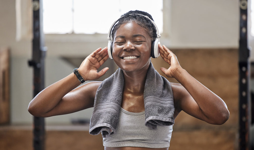 A fitness instructor is listening to a podcast in her headphones and smiling.