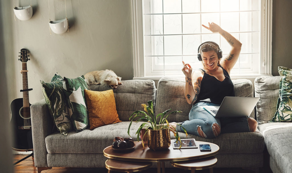 A dancer is listening to a podcast on their headphones and dancing on their couch at home.