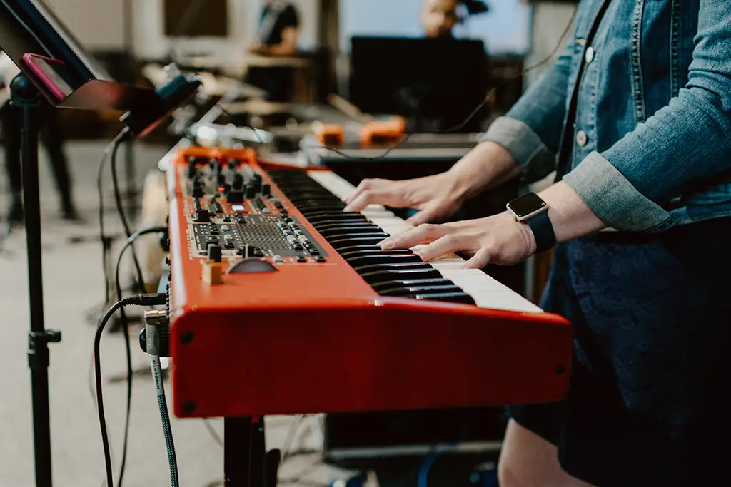 A close-up shot of a person playing a red electric keyboard with other musicians in the background.