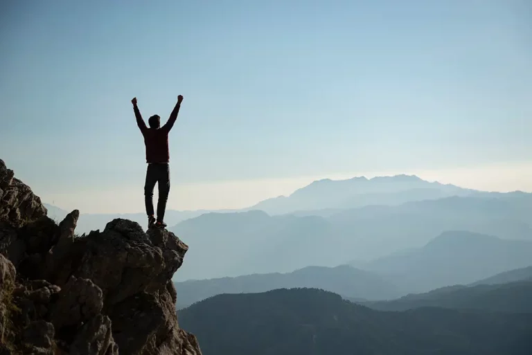 Person who climbed a mountain with their arms raised in excitement