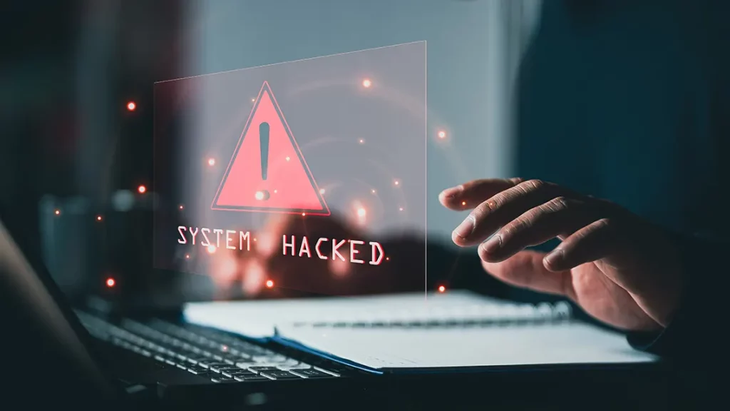 Image of person at a laptop with text overlay stating, "System Hacked."