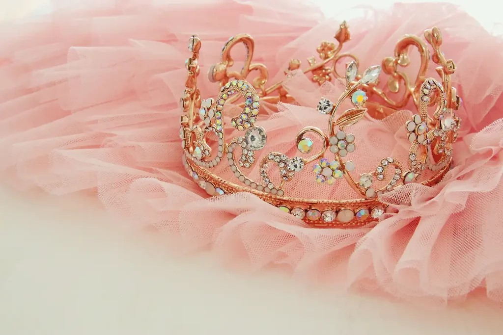 A close-up photo of a gold crown covered in rhinestones placed on top of pink tulle.