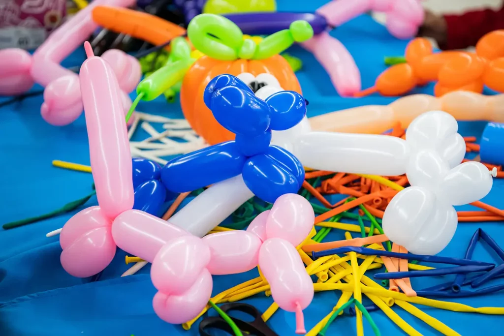 Several balloon animals in various colors including blue, pink, white and orange rest on top of a table covered in deflated balloons.