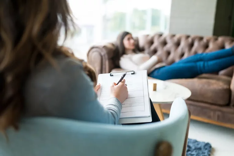 Therapist sitting in chair counseling patient laying on couch.