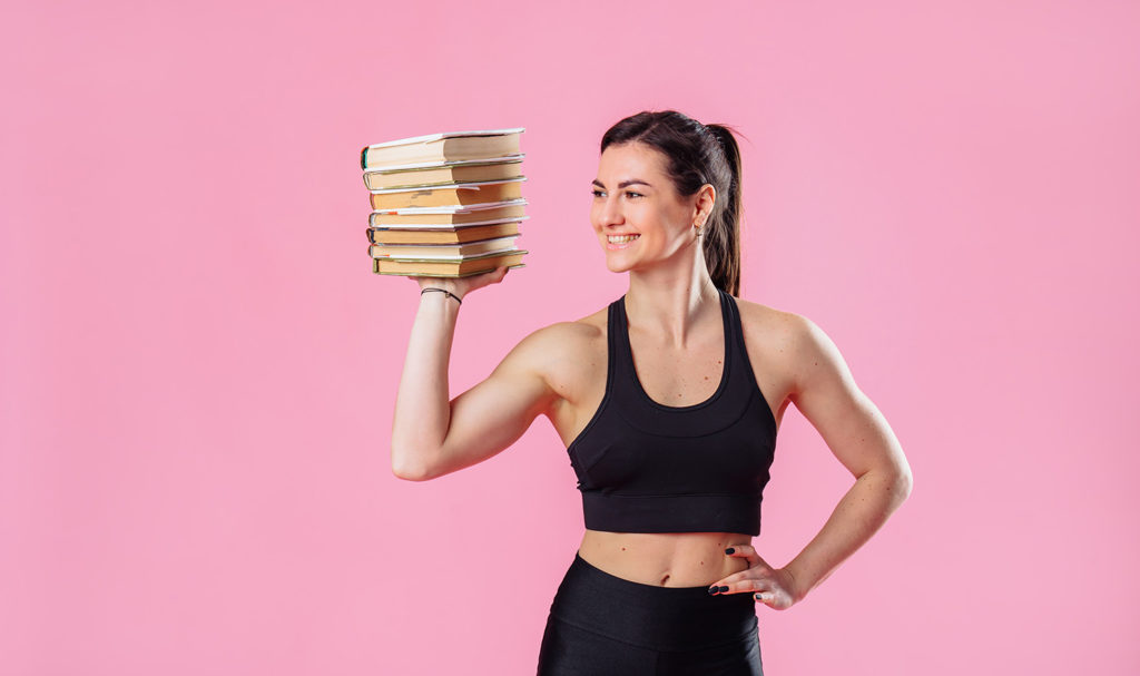 A personal trainer holding a stack of books against a pink background.