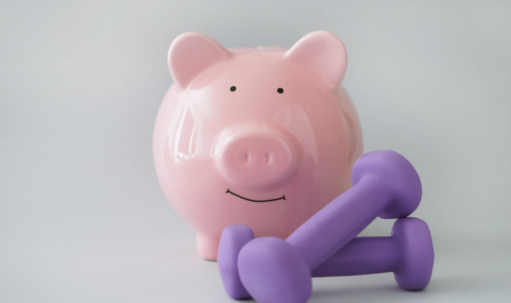 A piggy bank next to small purple hand weights on a gray background.