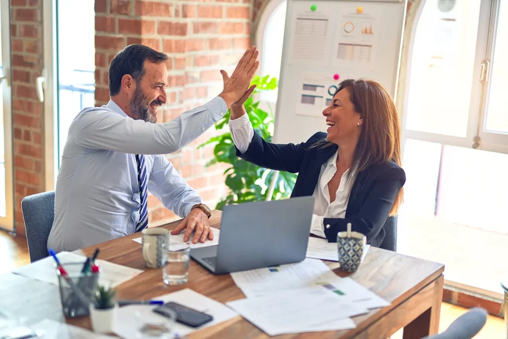 Two individuals in a business meeting high five with happy smiles