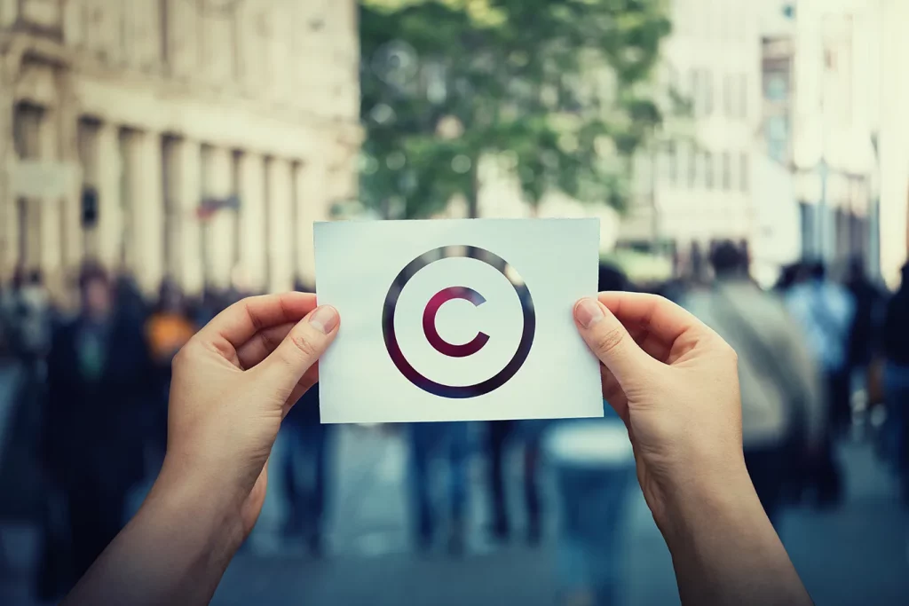 Copyright symbol cut out on paper being held in front of crowded walkway