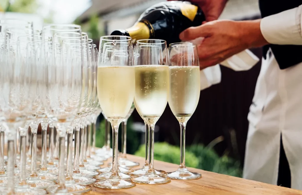 Person at a catered event pouring champagne glasses.