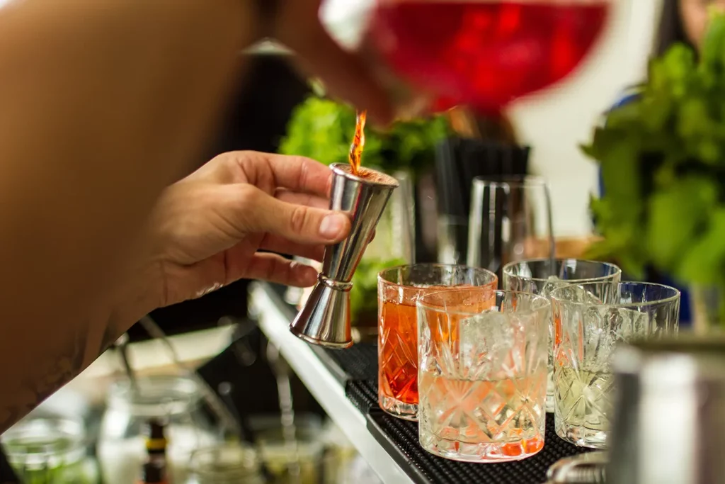 A close-up shot of a person pouring liquor into a jigger before adding it to a cocktail.