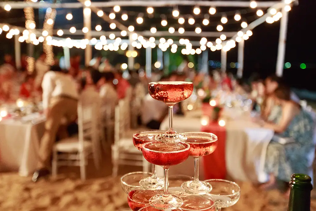 A pyramid made of glasses of pink champagne on display at an outdoor wedding.