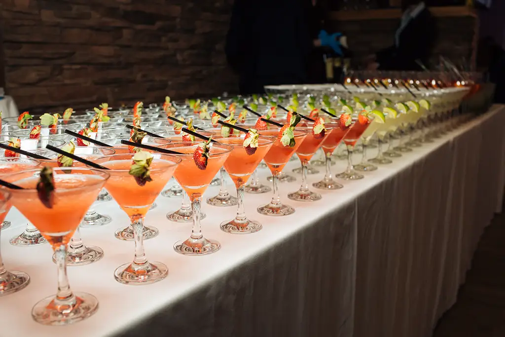 A table at an event filled with a variety of different cocktails garnished with various fruits.