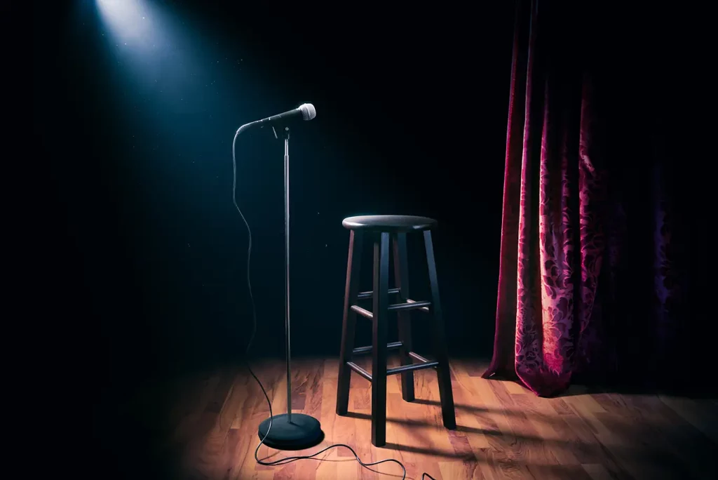 A spotlight shines on a microphone and stool on an empty stage.