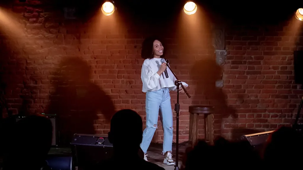 A woman performs a comedy routine on stage at a small club.