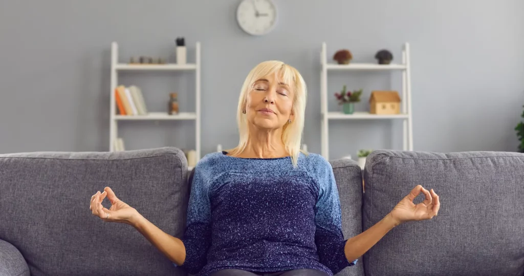 A lady sitting on a couch in a meditative pose.