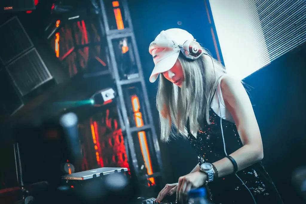 A DJ with long silver hair performing on stage at an event.