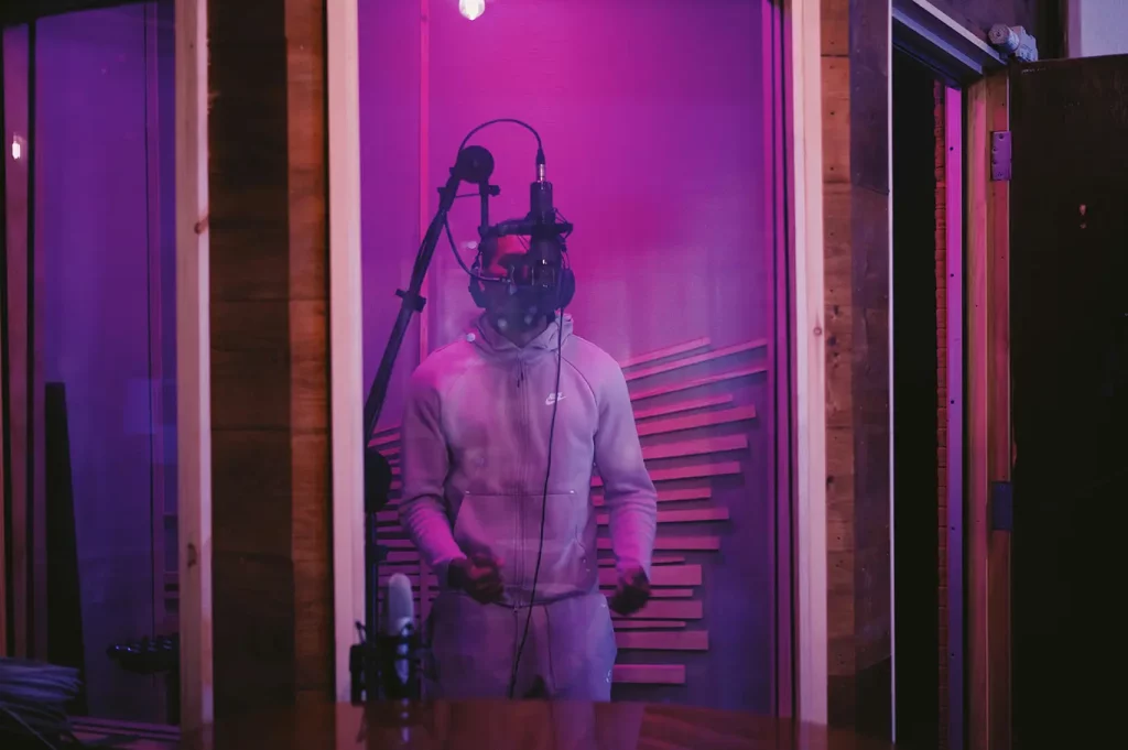 A person records vocals in a studio booth lit by purple lights.