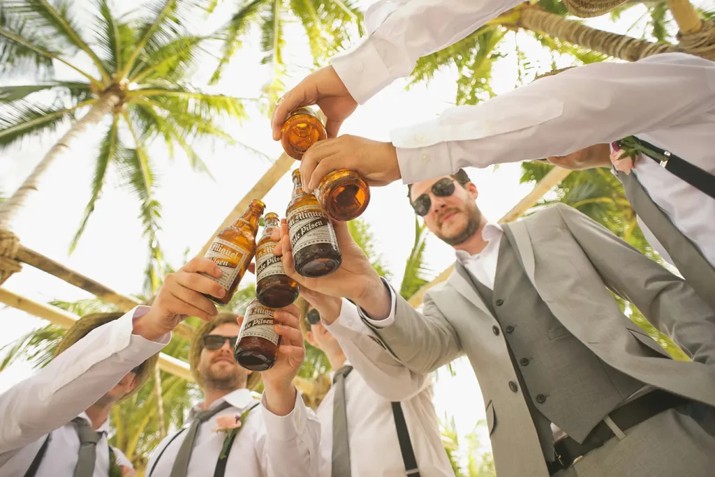 A group of men at a wedding holding bottles of beer together.