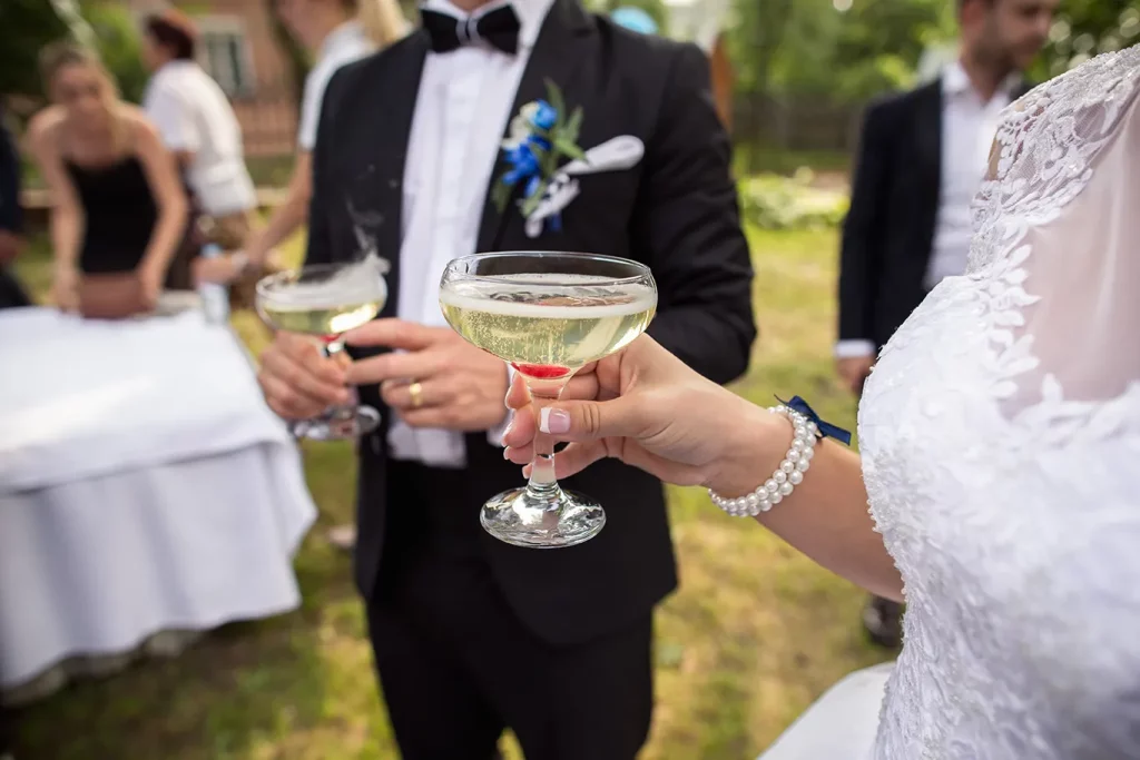 A bride and a groom hold glasses of champagne at an outdoor wedding reception.