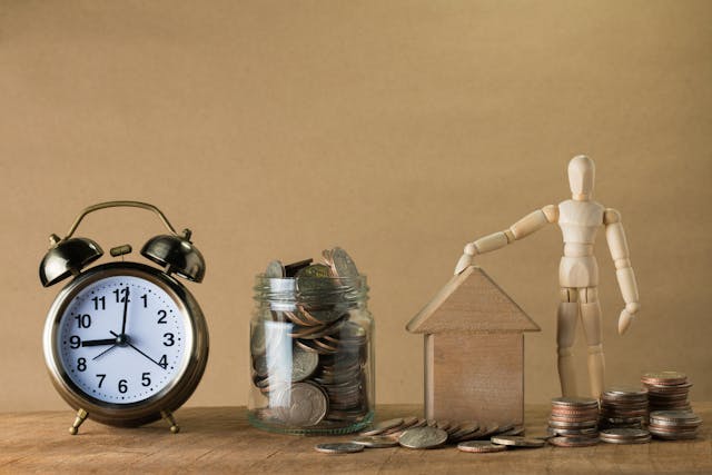 a clock, a cup of coins, a block house, and a small wooden mannequin