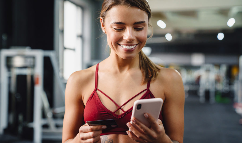 A personal trainer is smiling while holding her phone in the gym.