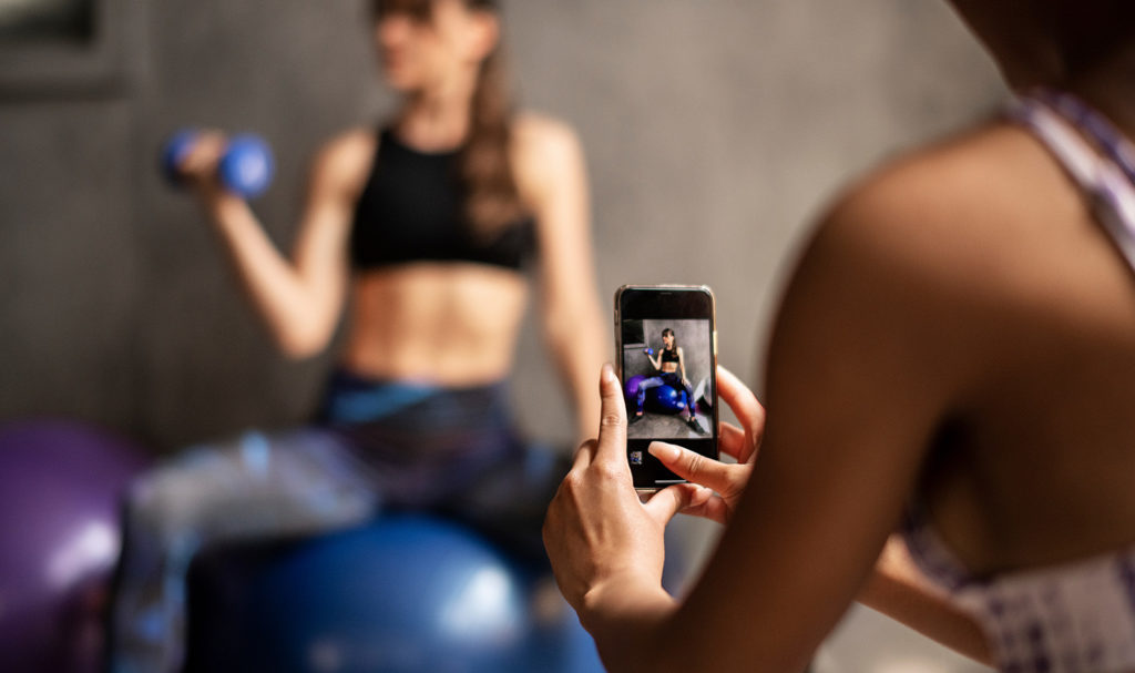 A close-up shot focusing on a smart phone a trainer is using to capture a workout video of another personal trainer.