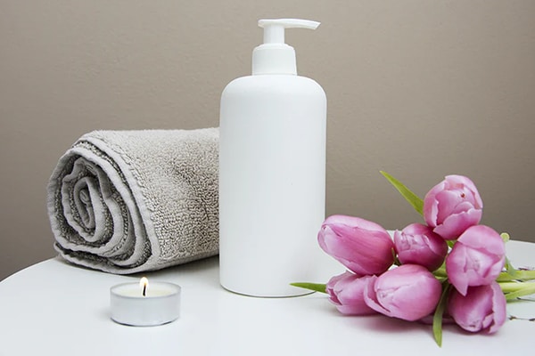 Cosmetic cream on a table with a towel, a candle, and some flowers.