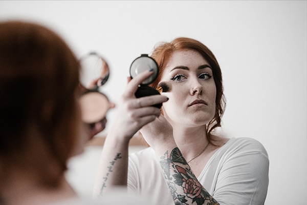A woman applies makeup in a mirror.
