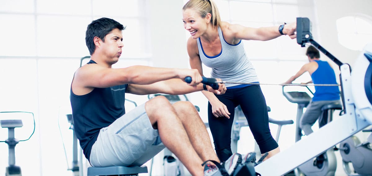 Female personal trainer works with male client on a rowing machine.