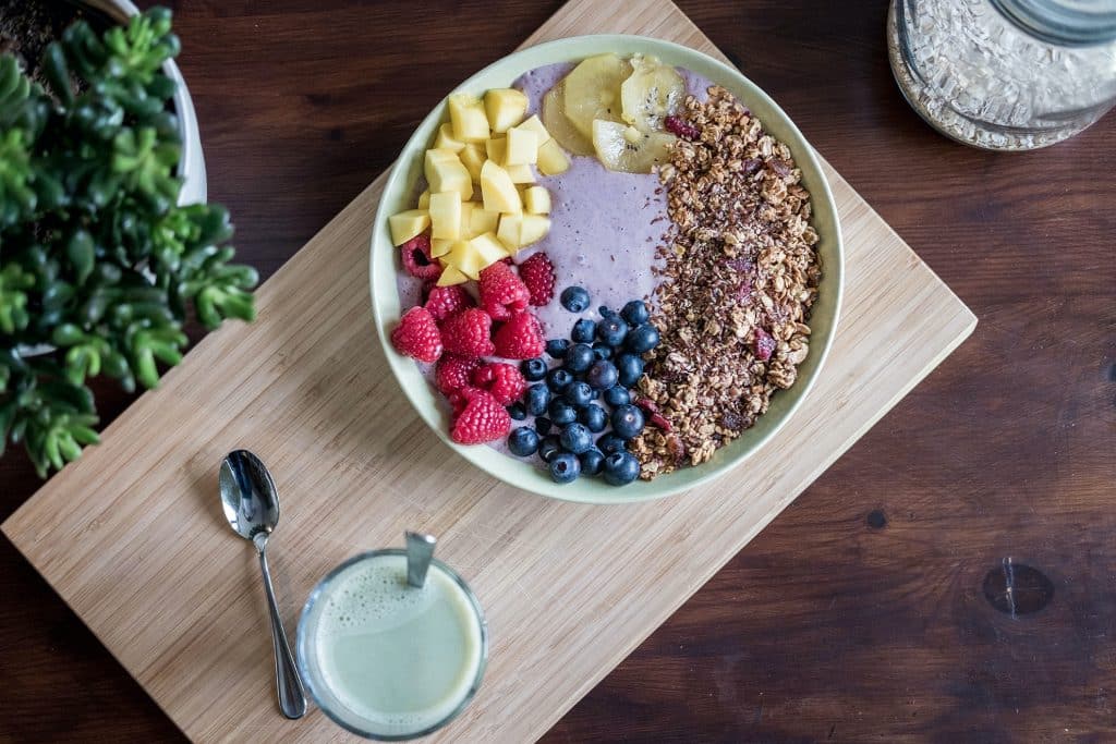 A bowl of fruits, yogurt, and granola on a cutting board.