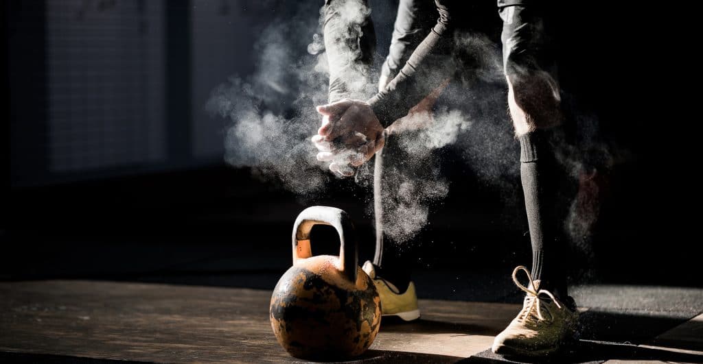An athlete prepares to lift a kettle bell with chalk.