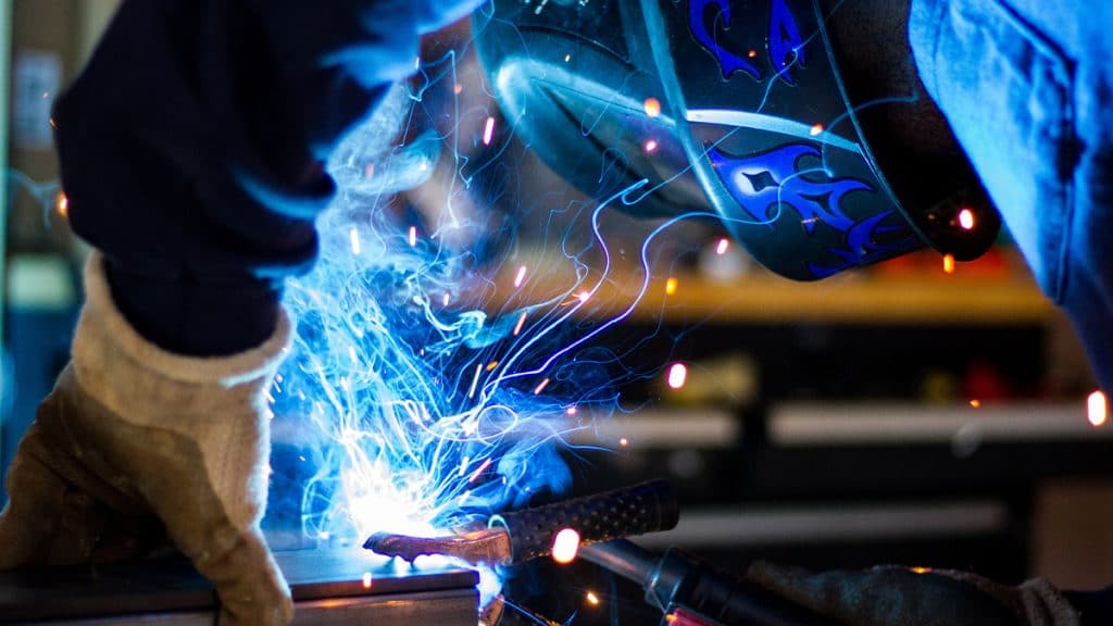 blue smoke and bright sparks fly as a welder works.