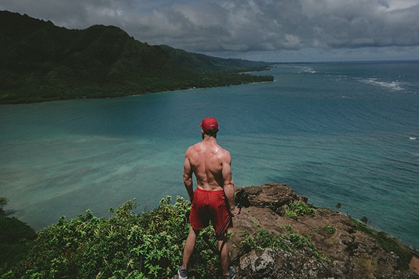 A strong man stands in nature over the ocean, with large muscles built with the help of vitamin supplements that have been insured with supplement liability insurance.