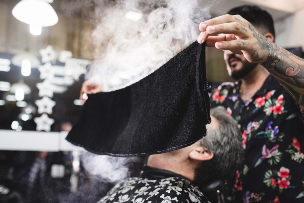 Barber placing warm towel on man's face