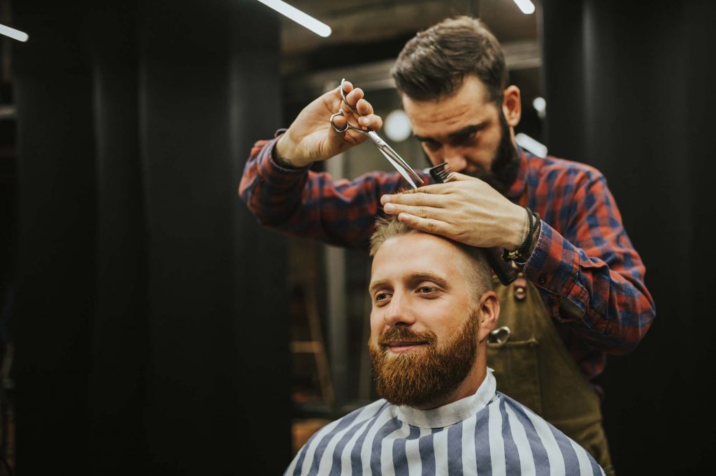 Barber cutting man's hair with scissors