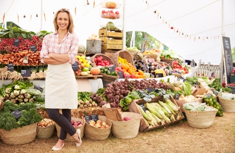 woman standing in front of famers market vegetable stand