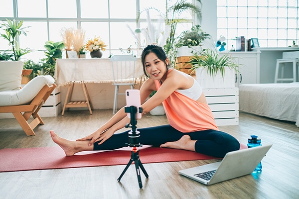 A woman records herself teaching a yoga class from her home, which is a teaching style covered by her yoga insurance.