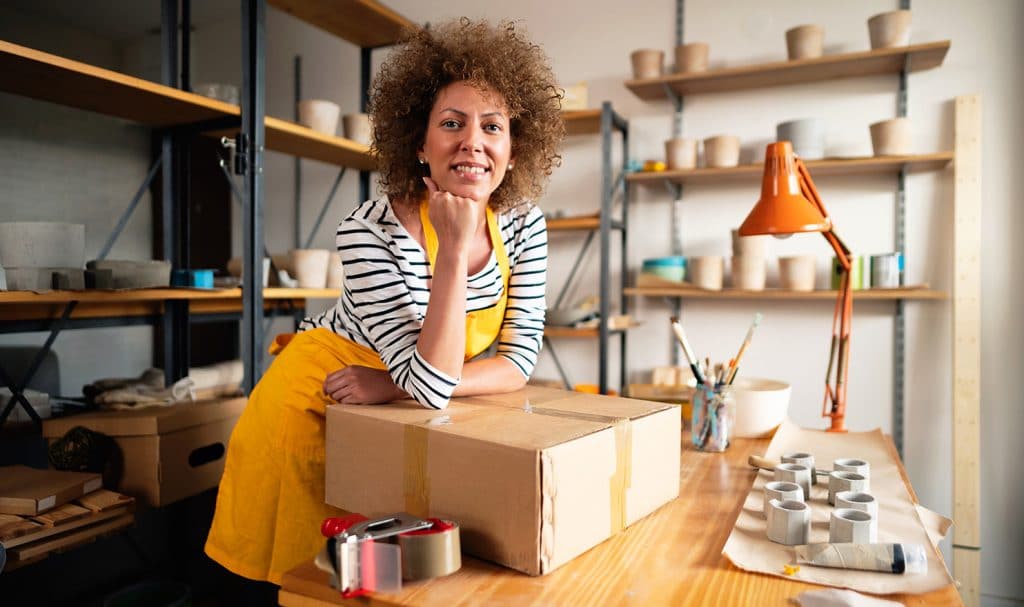 A woman proudly poses with a package she is ready to ship, and she is confident her pottery product are safe because she has product liability insurance.