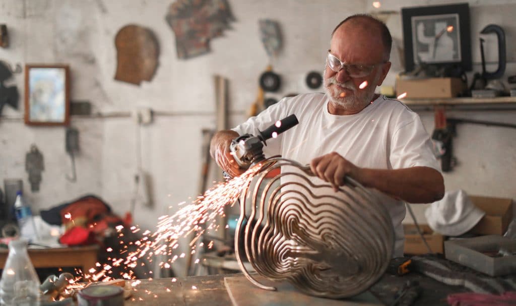 A man confidently works on a metal piece in his home studio, which is covered with etsy seller insurance.