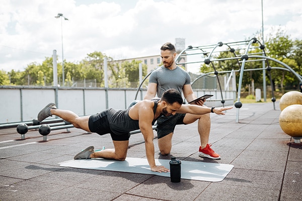 Personal trainer assesses their client’s balance as they do a workout on a mat.