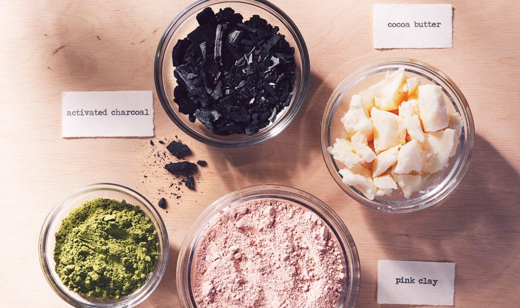 Various beauty product ingredients are places in jars and set on top of a woof table with labels next to them.