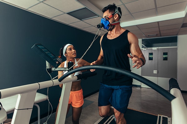 An exercise physiologist helps her client track his breathing and heart rate with machines as he uses the treadmill.