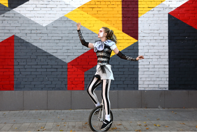 woman clown on unicycle in front of cool mural